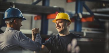 Happy worker greeting his manager with a handshake in an aluminum mill.