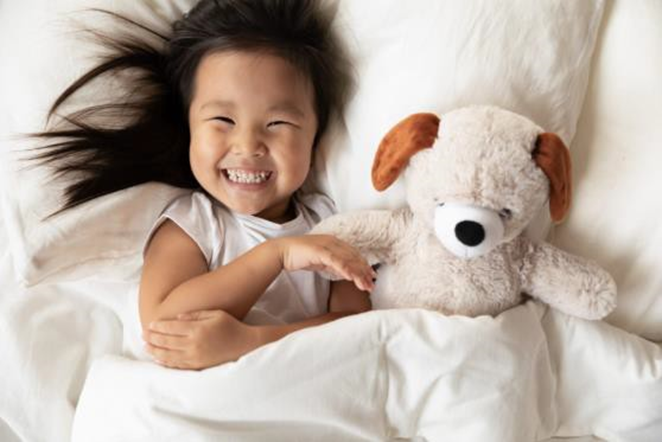 girl in bed smiling and  playing with stuffed toy