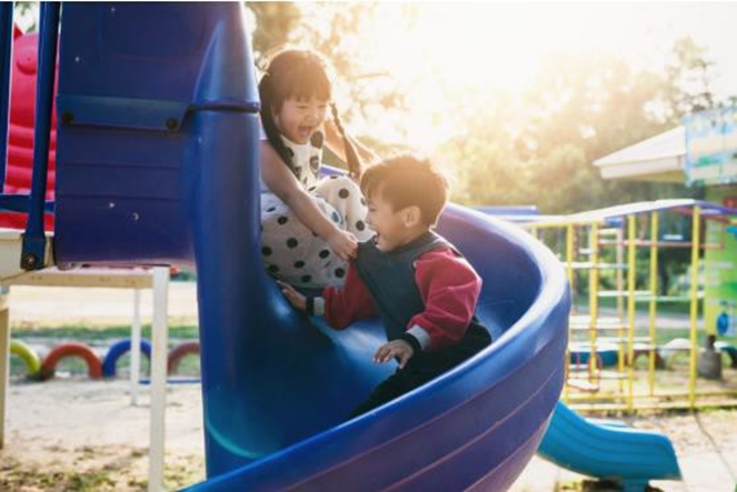 girl and boy going down a slide in a playground