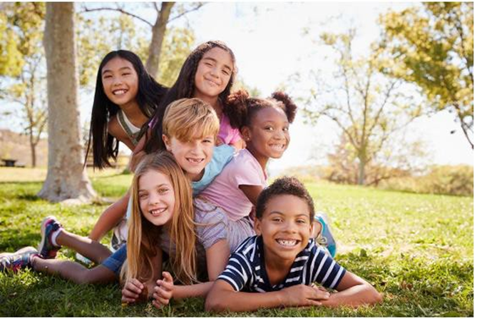 Group of kids on top of each other on the grass smiling for the camera