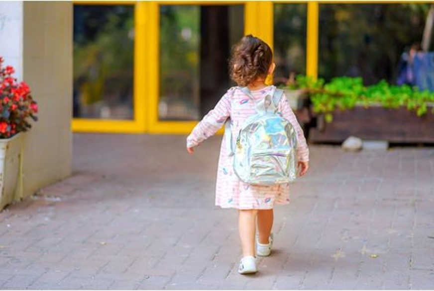 little girl carrying a backpack and walking towards the door