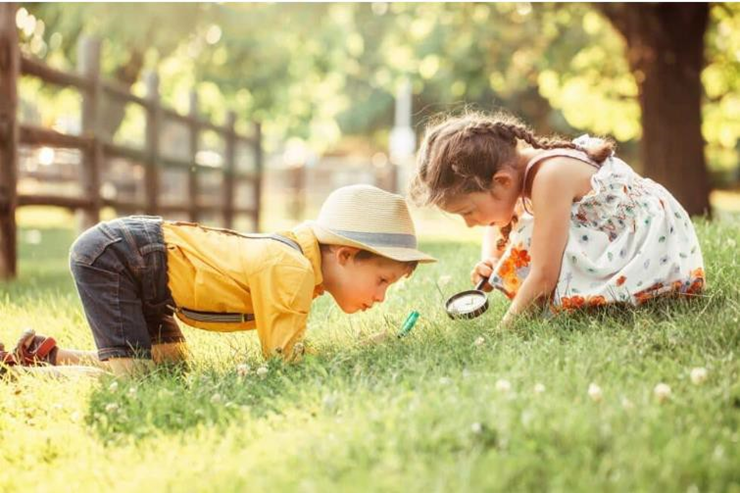 2 kids with magnifying glasses searching for something on the grass