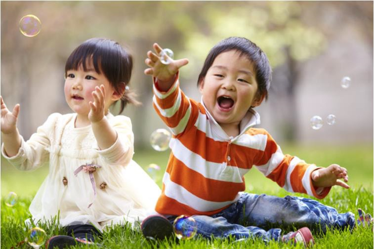 girl and boy sitting on the grass  playing with bubbles